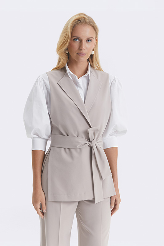 A stylish Natali Bolgar women's look: a beige wrap vest that defines the waist, a white shirt, and elegant trousers.