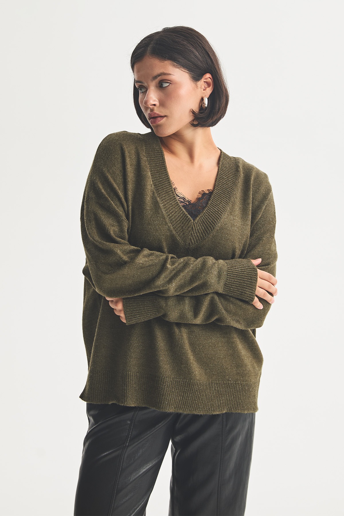 Оливковий светр вільного крою з V-подібним вирізом і трикотажними манжетами, під ним мереживний топ, із шкіряними штанами